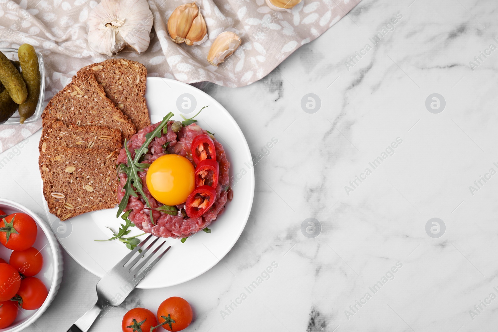 Photo of Tasty beef steak tartare served with yolk and other accompaniments on white marble table, flat lay. Space for text