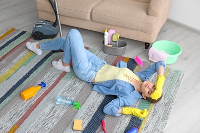 Photo of Tired woman with cleaning supplies lying on carpet at home