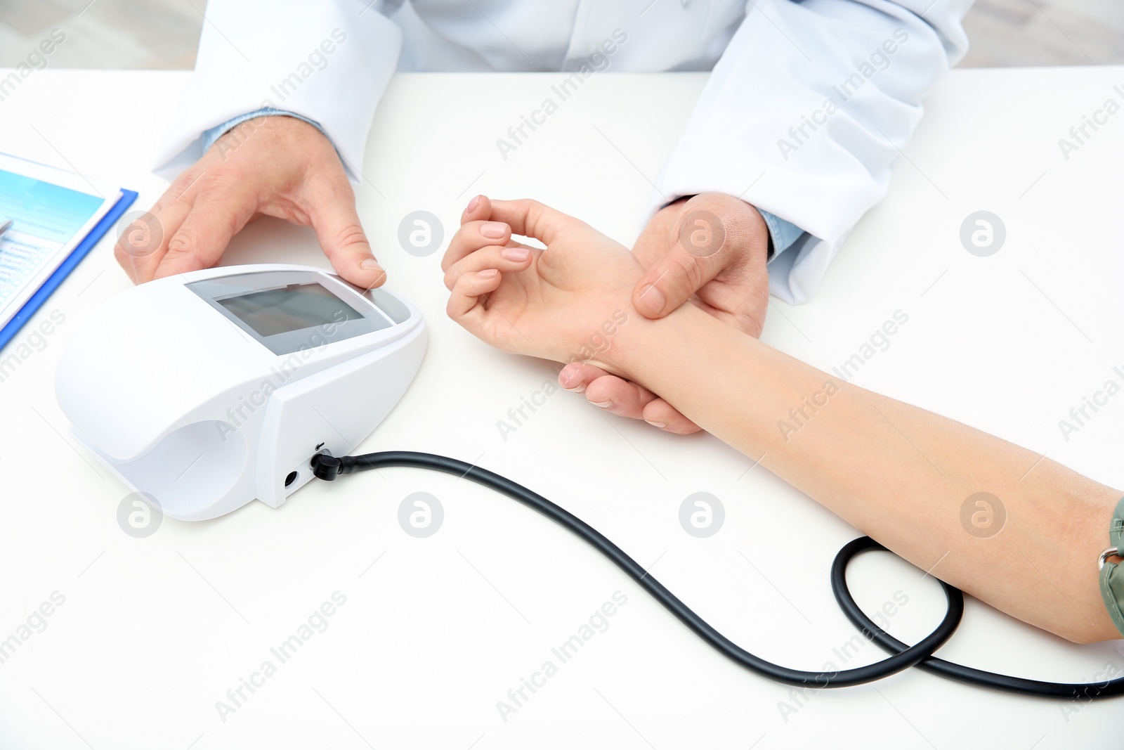 Photo of Doctor checking young woman's pulse and measuring blood pressure at table in hospital, closeup