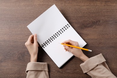 Photo of Woman writing in notebook at wooden table, top view