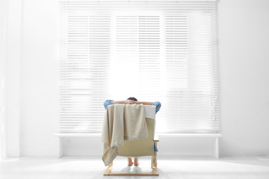 Photo of Young woman relaxing in armchair near window at home, back view