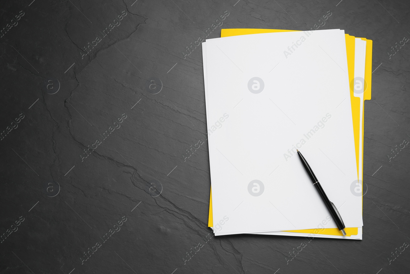 Photo of Yellow file with blank sheets of paper and pen on black slate table, top view. Space for text