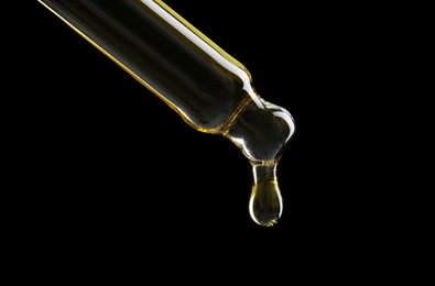 Photo of Dripping tincture from pipette on black background, closeup