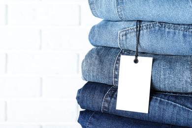 Stack of different jeans near white brick wall, closeup. Space for text