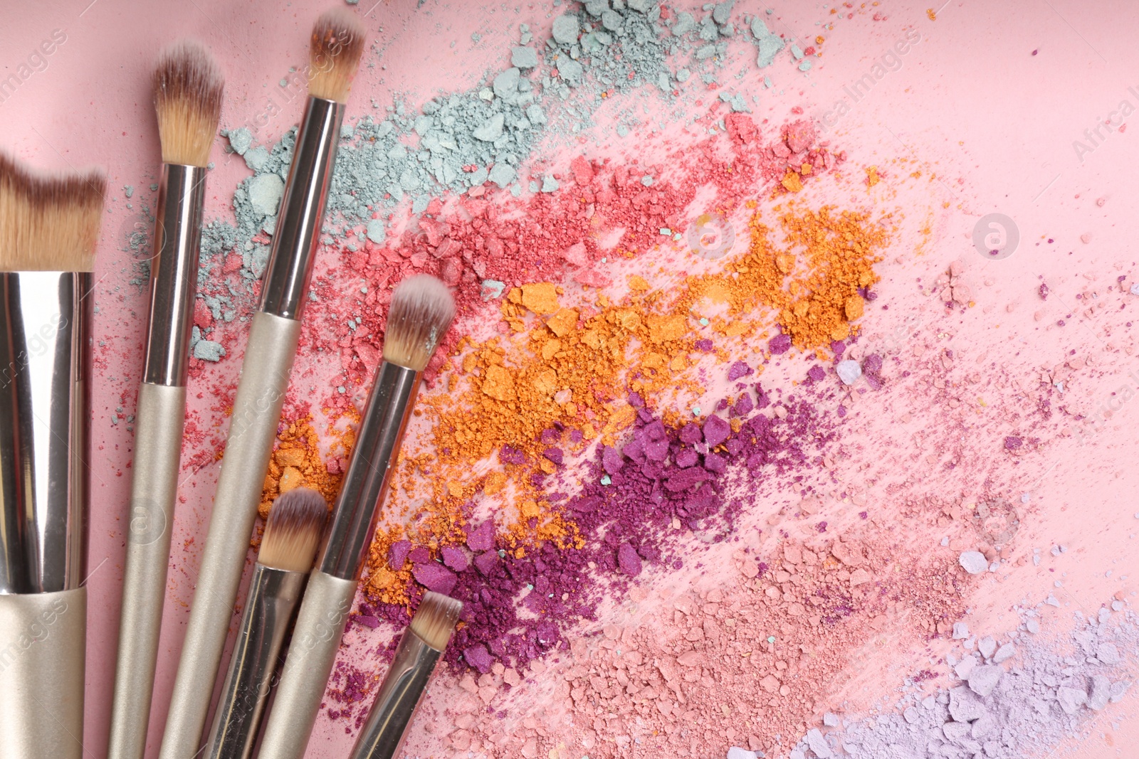 Photo of Makeup brushes and scattered eye shadows on pink background, flat lay