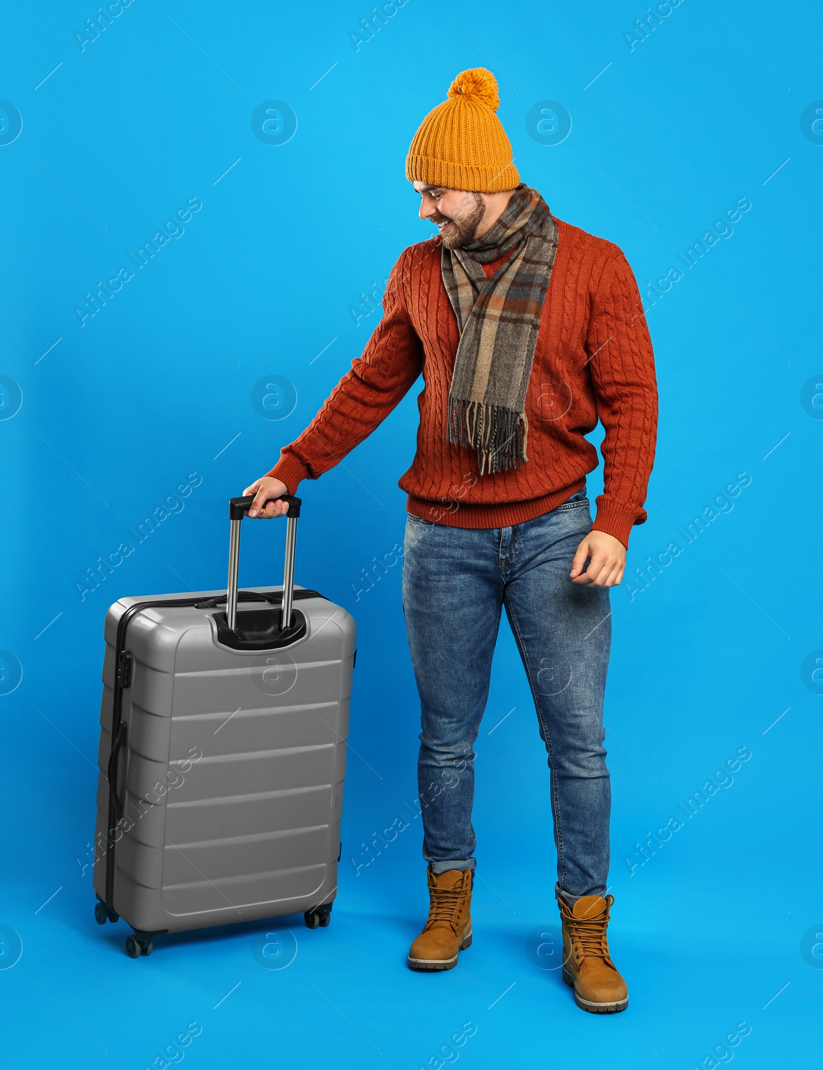 Photo of Young man in warm clothes with suitcase on blue background. Winter vacation