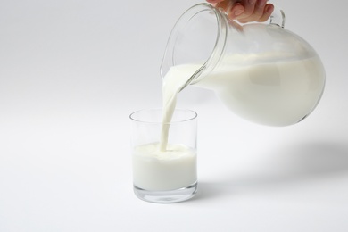 Photo of Woman pouring milk into glass on white background, closeup