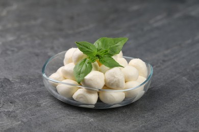 Tasty mozzarella balls and basil leaves in bowl on grey table