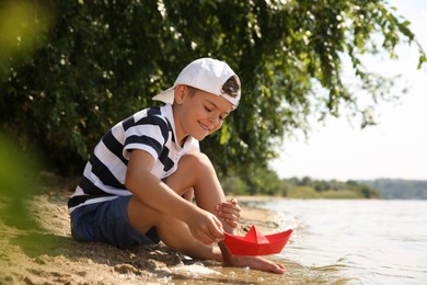 Photo of Cute little boy playing with paper boat near river