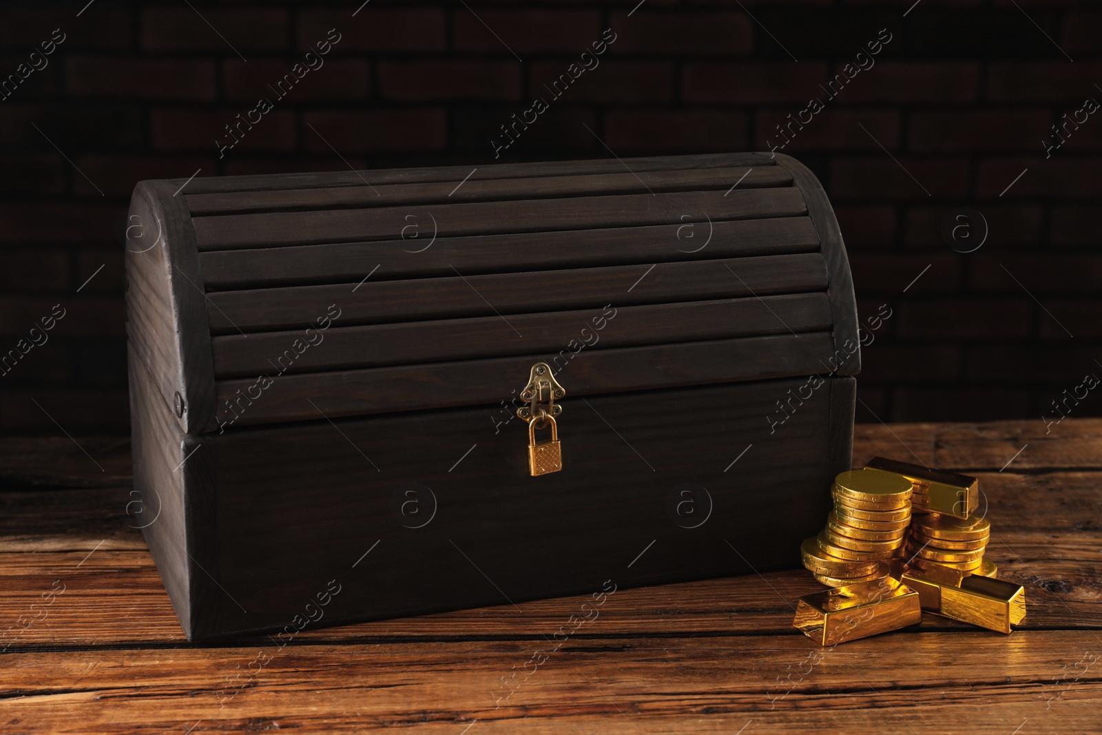 Photo of Closed treasure chest with lock, gold bars and coins on wooden table
