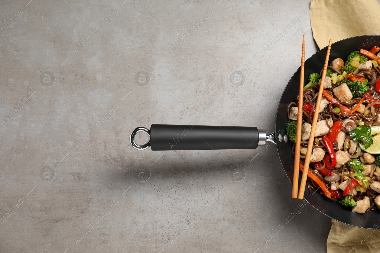 Photo of Stir-fry. Tasty noodles with meat in wok and chopsticks on grey textured table, top view. Space for text