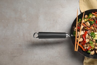 Photo of Stir-fry. Tasty noodles with meat in wok and chopsticks on grey textured table, top view. Space for text