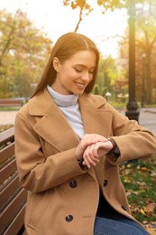 Photo of Beautiful young woman wearing stylish clothes on bench in autumn park