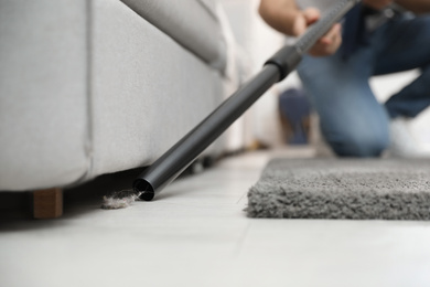 Young man using vacuum cleaner at home, closeup