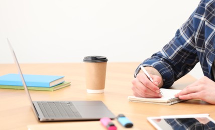 Photo of E-learning. Man taking notes during online lesson on table indoors, closeup