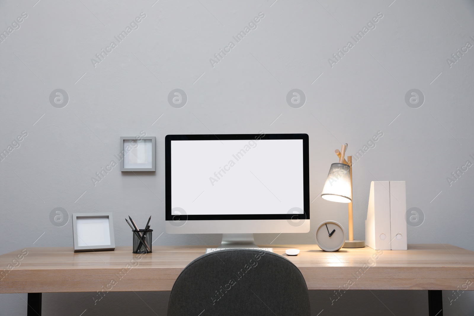 Photo of Comfortable workplace with blank computer display on desk near light grey wall. Space for text