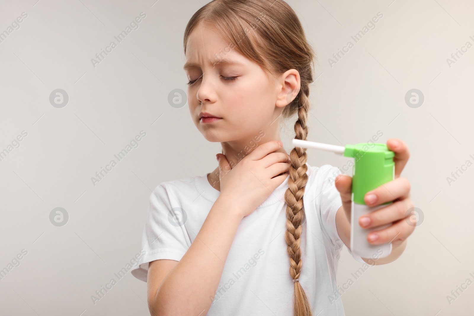 Photo of Little girl holding throat spray on light grey background