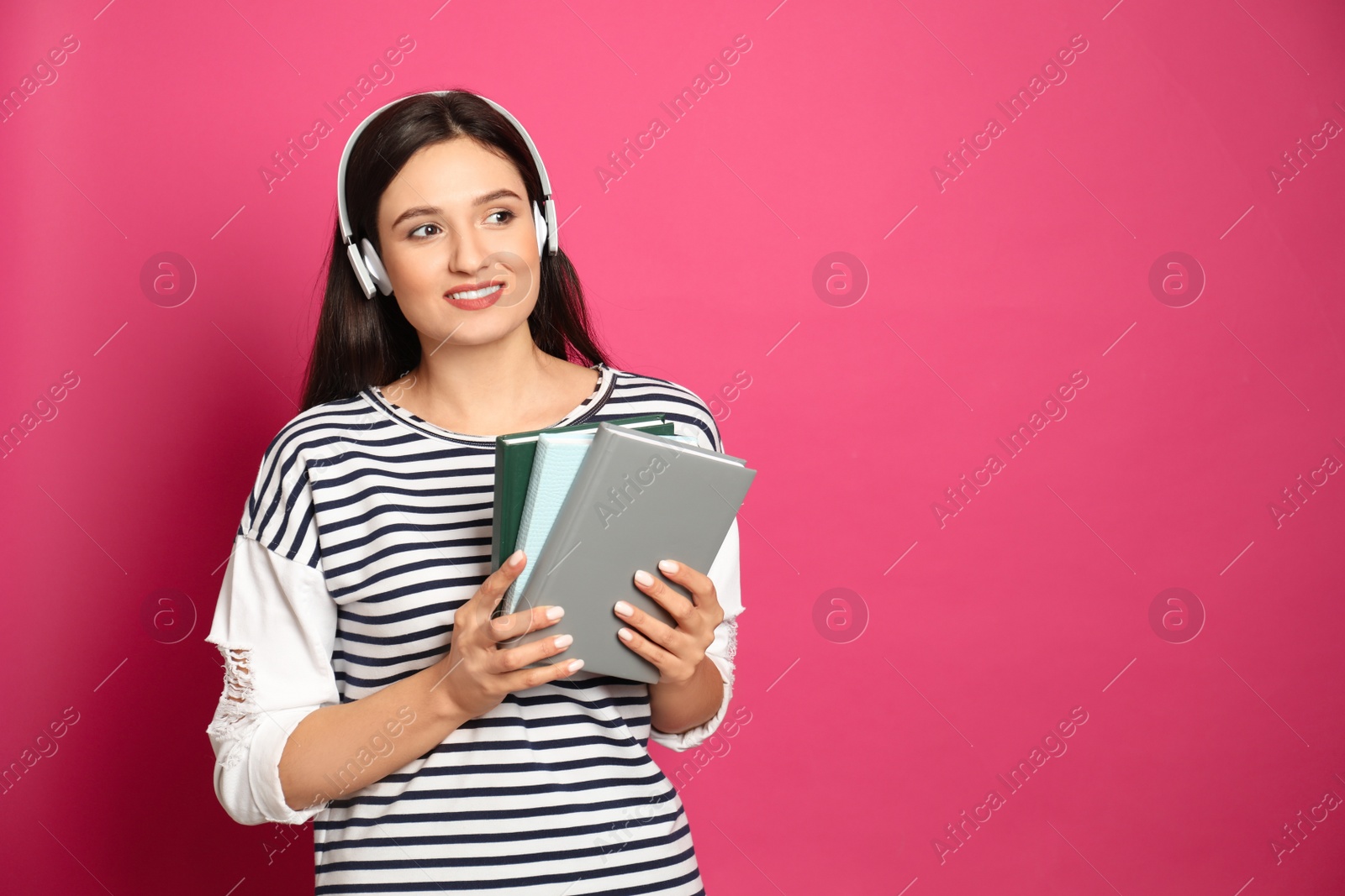 Photo of Young woman listening to audiobook on pink background. Space for text