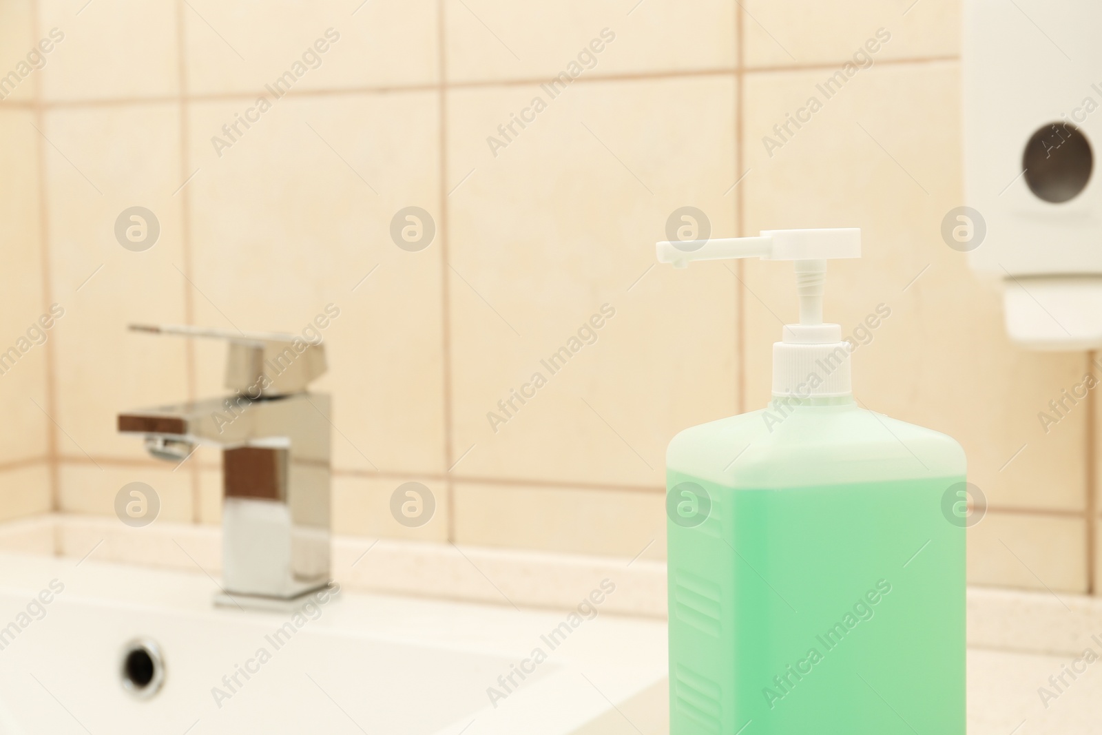 Photo of Dispenser bottle with antiseptic gel in public bathroom. Space for text