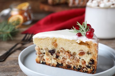 Photo of Slicetraditional Christmas cake decorated with rosemary and cranberries on table, closeup