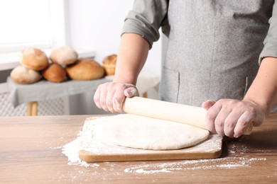 Man rolling dough at table in kitchen, closeup