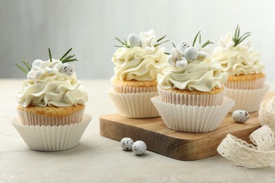 Photo of Tasty Easter cupcakes with vanilla cream and candies on gray table