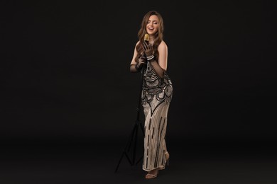 Photo of Beautiful young woman in stylish dress with microphone singing on black background