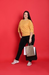 Photo of Beautiful overweight woman with shopping bags on red background