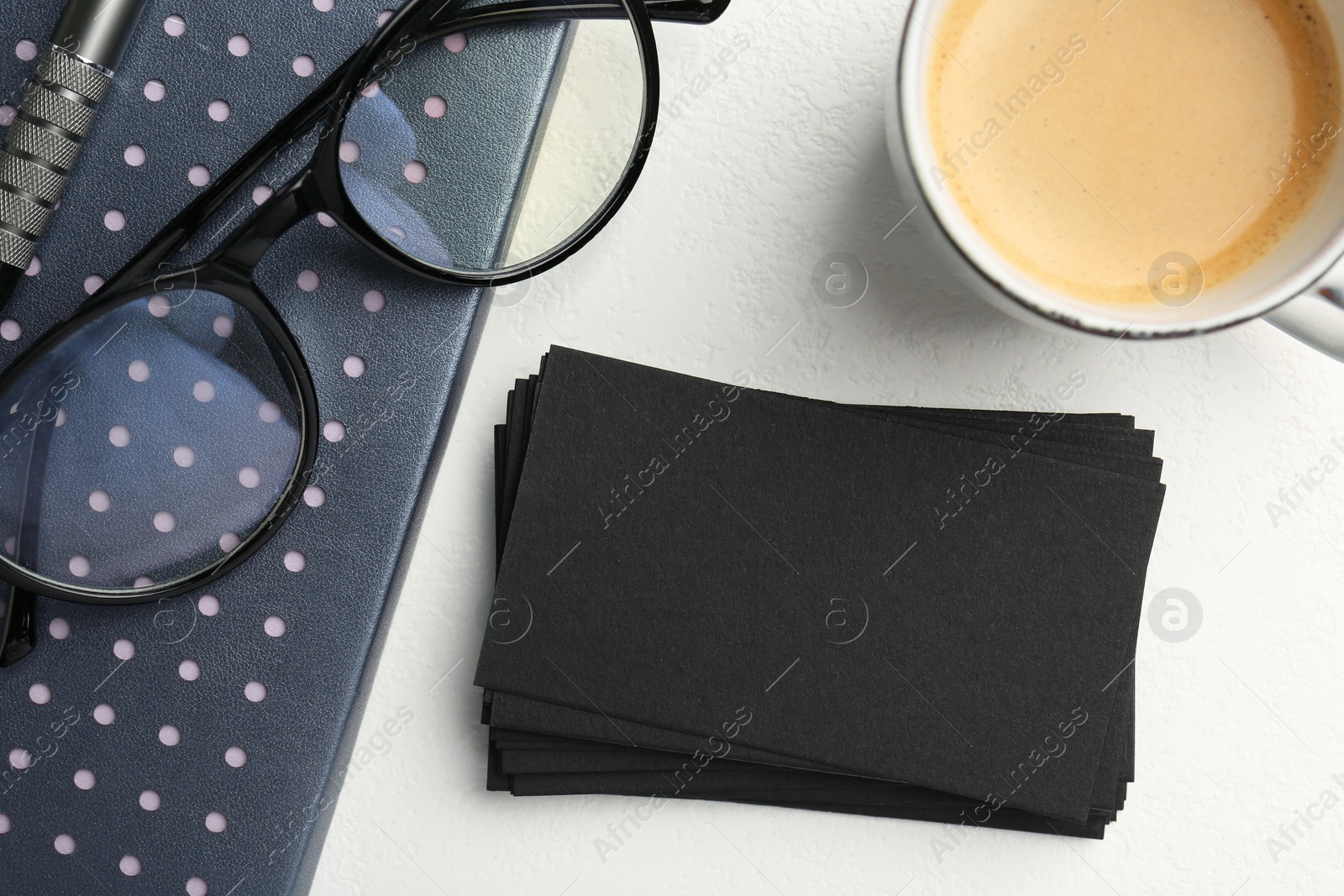 Photo of Blank black business cards, cup of coffee, glasses and stationery on white table, top view. Mockup for design