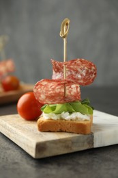 Photo of Tasty canape with salami, greens, cream cheese and tomato on grey table