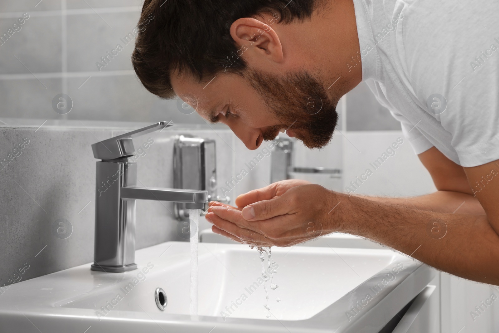 Photo of Handsome bearded man washing over sink in bathroom