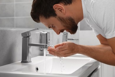 Photo of Handsome bearded man washing over sink in bathroom