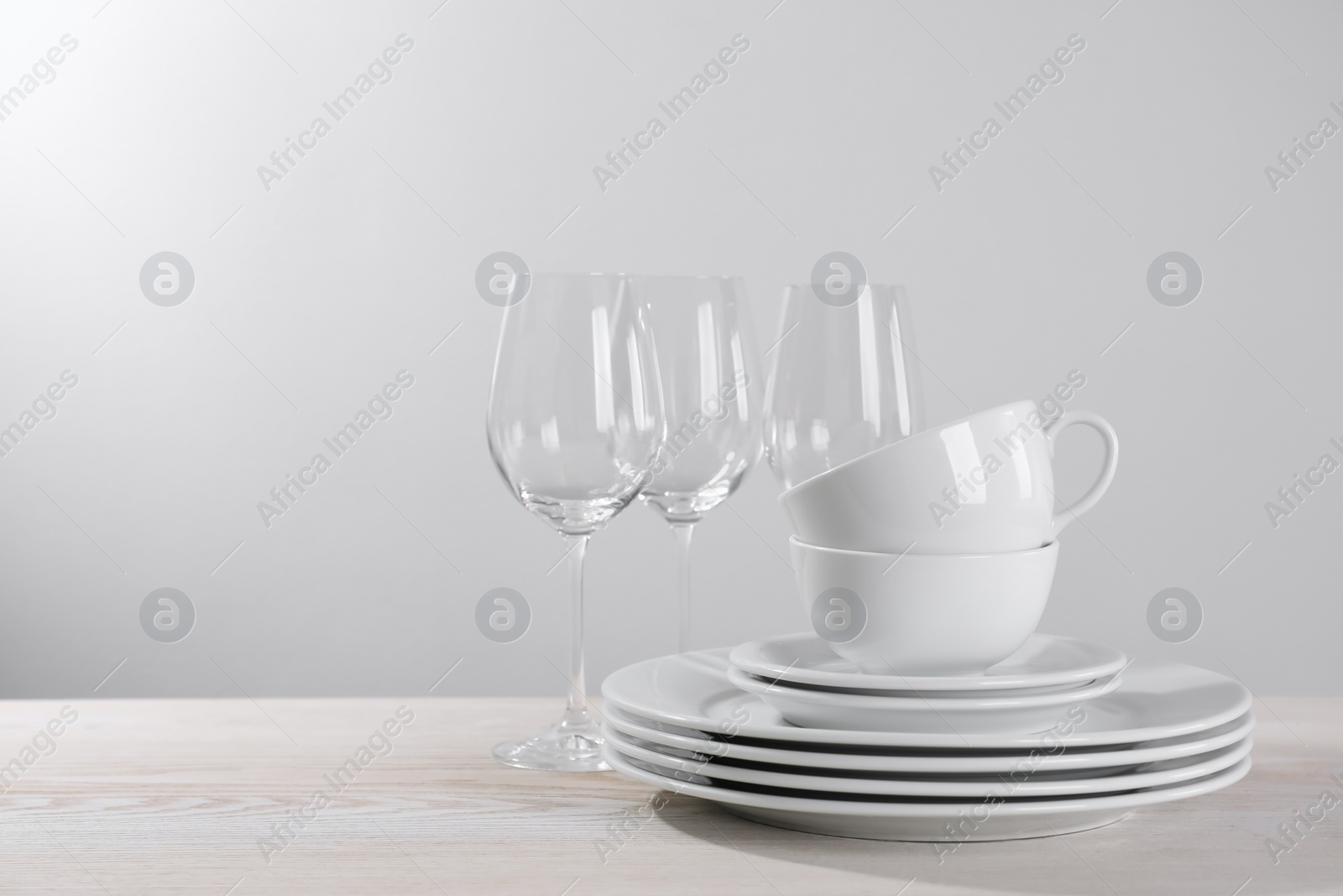 Photo of Set of clean dishware and glasses on white wooden table against light background. Space for text