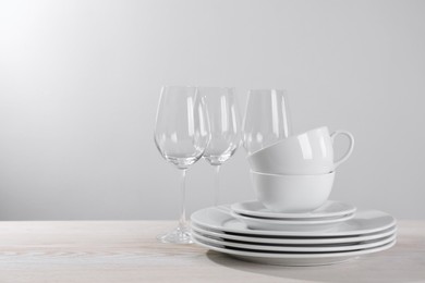 Set of clean dishware and glasses on white wooden table against light background. Space for text