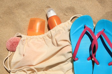 Photo of Sunscreens, seashell and beach accessories on sand, flat lay