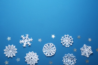 Photo of Flat lay composition with paper snowflakes on blue background, space for text. Winter season