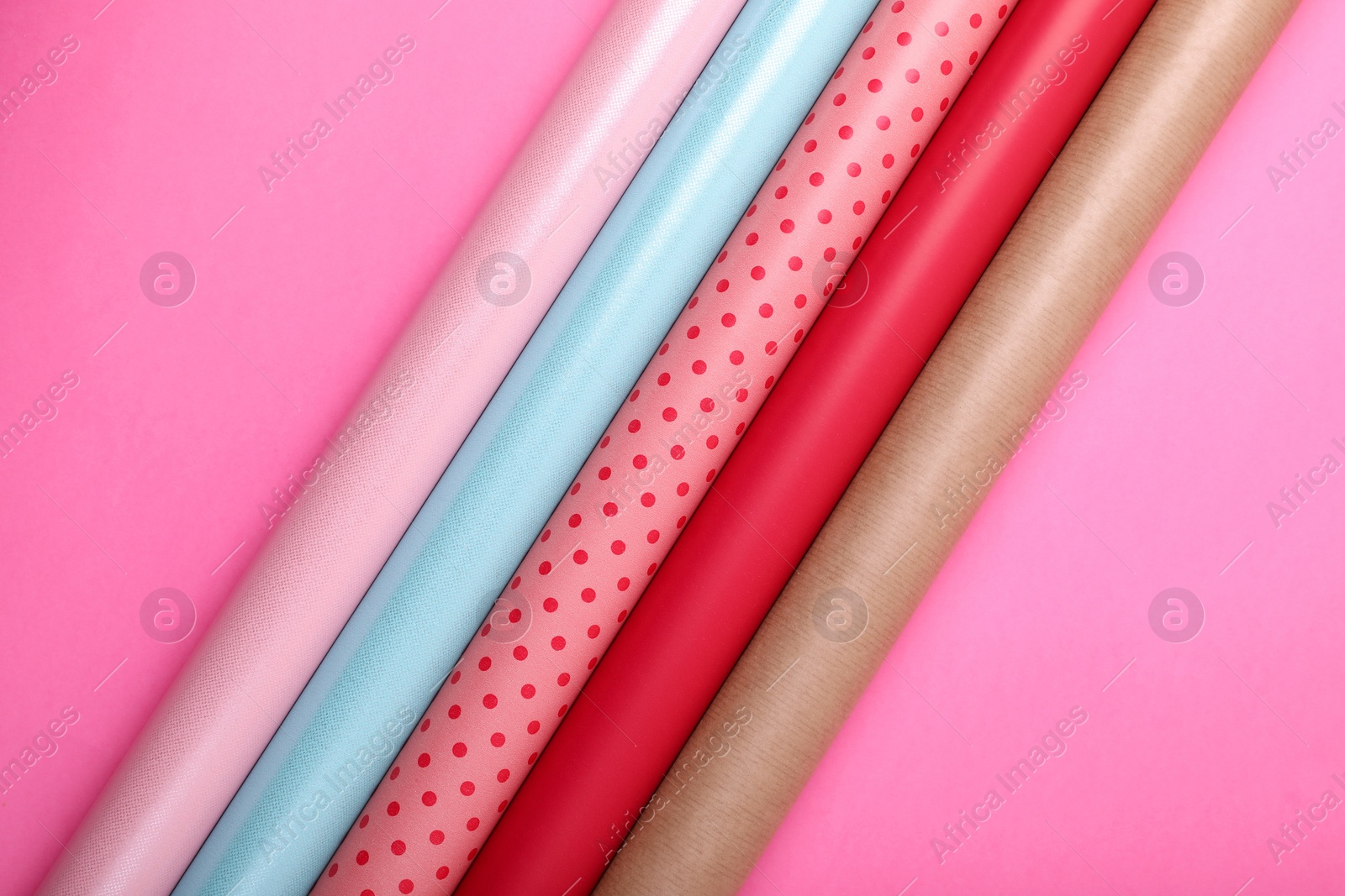 Photo of Rolls of colorful wrapping paper on pink background, flat lay