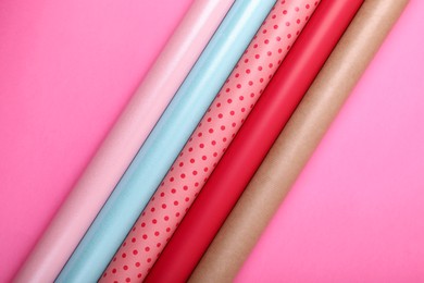 Photo of Rolls of colorful wrapping paper on pink background, flat lay