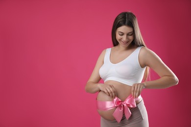 Photo of Young pregnant woman with bow on her belly against pink background, space for text. Time to give birth