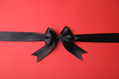 Photo of Black satin ribbon with bow on red background, top view