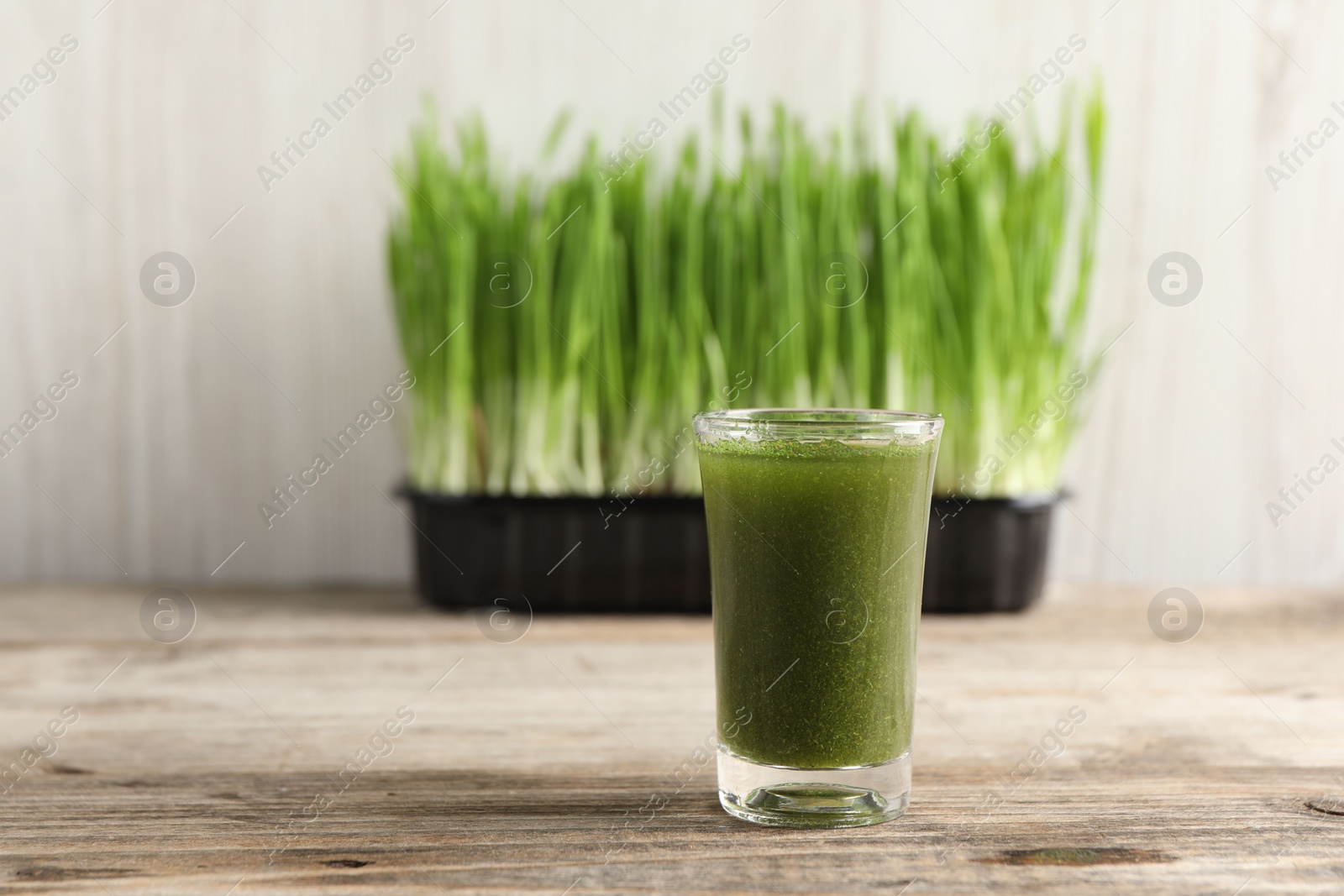 Photo of Wheat grass drink in shot glass on wooden table, closeup. Space for text