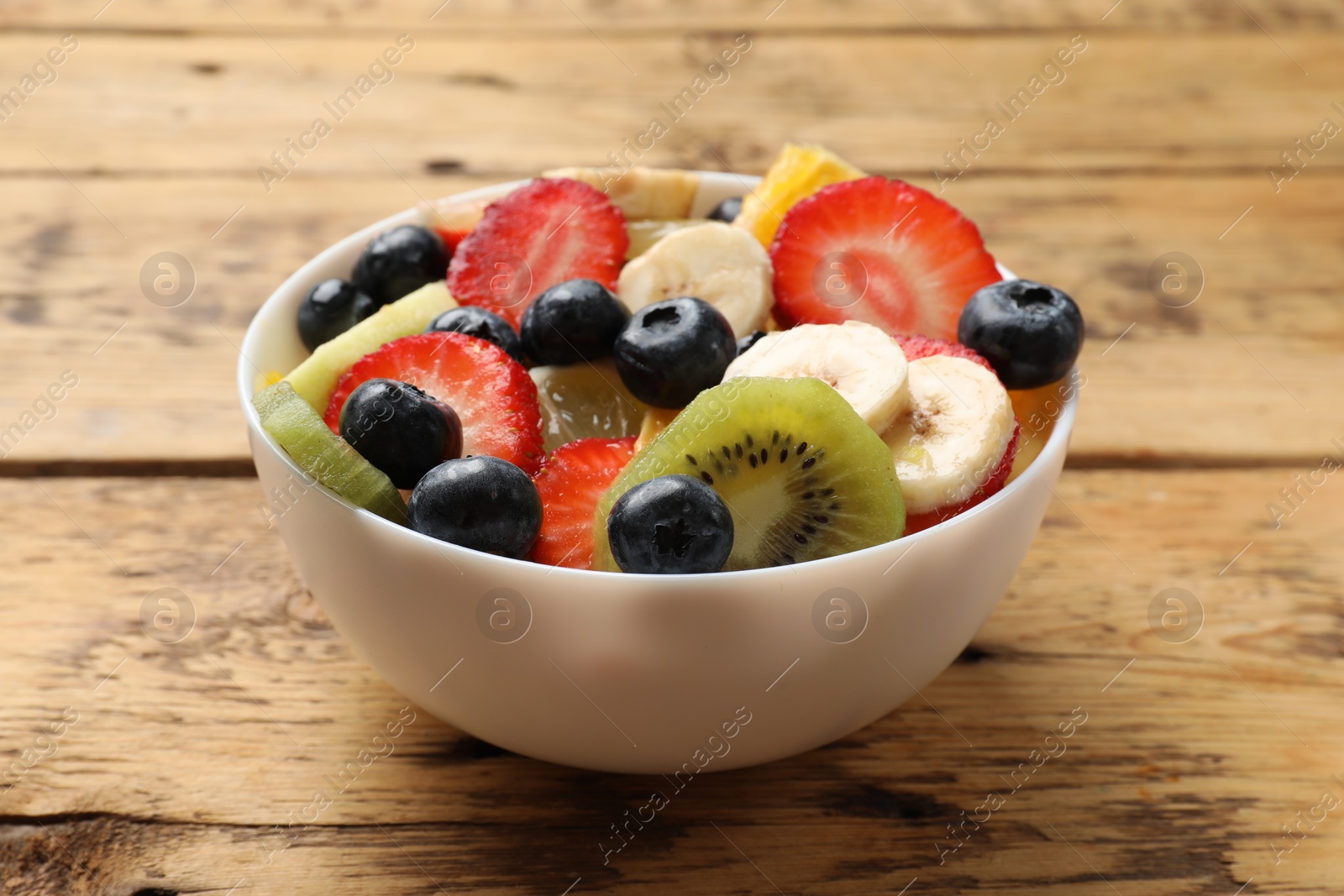 Photo of Tasty fruit salad in bowl on wooden table, closeup