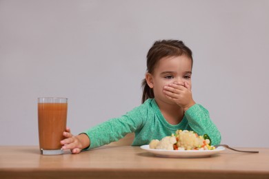 Photo of Cute little girl covering mouth and refusing to drink juice at table on grey background