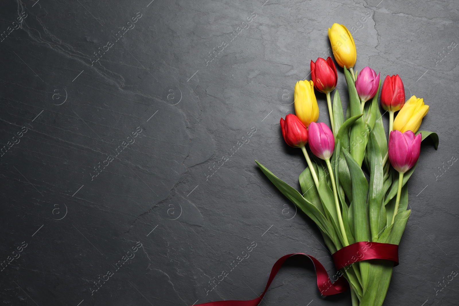 Photo of Beautiful colorful tulip flowers and ribbon on black table, flat lay. Space for text