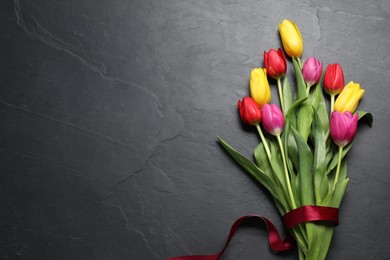 Beautiful colorful tulip flowers and ribbon on black table, flat lay. Space for text