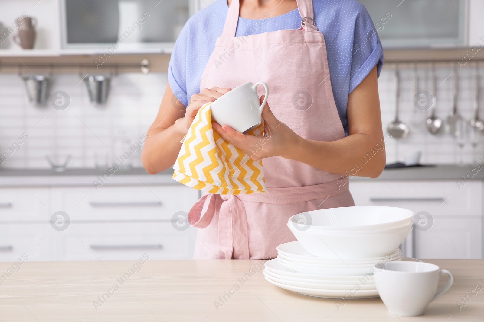 Photo of Woman wiping ceramic cup at table with clean dishes in kitchen, closeup