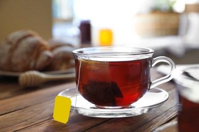Photo of Tea bag in glass cup on wooden table indoors, closeup