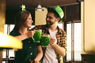 Photo of Young man and woman toasting with green beer in pub. St. Patrick's Day celebration