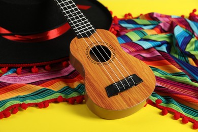 Black Flamenco hat, poncho and ukulele on yellow table, closeup