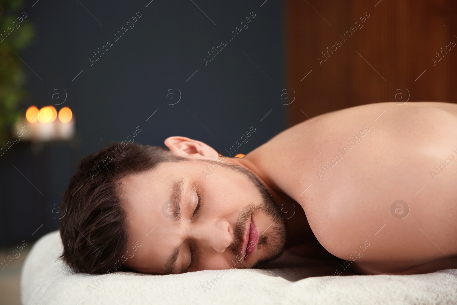 Photo of Handsome man relaxing on massage table in spa salon